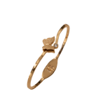 A gold-plated bangle bracelet with a small butterfly charm and a tiny clear stone, shown on a plain white background.