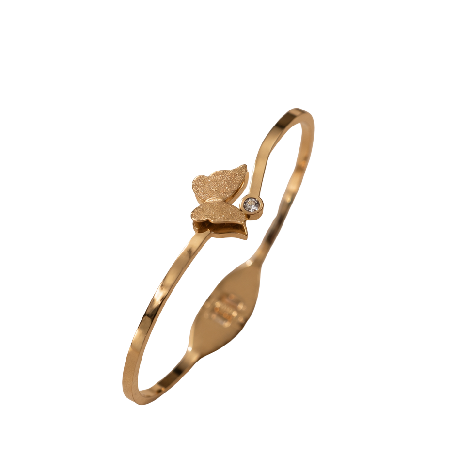 A gold-plated bangle bracelet with a small butterfly charm and a tiny clear stone, shown on a plain white background.