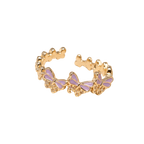 A gold-plated open ring band decorated with a row of small butterfly charms featuring light purple enamel wings, set against a plain white background.