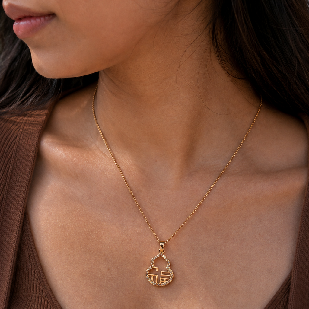 A close-up of a model wearing a delicate gold chain necklace with a small pendant featuring a stylized Chinese character, paired with a brown ribbed top.