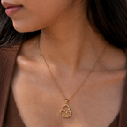 A close-up of a model wearing a delicate gold chain necklace with a small pendant featuring a stylized Chinese character, paired with a brown ribbed top.