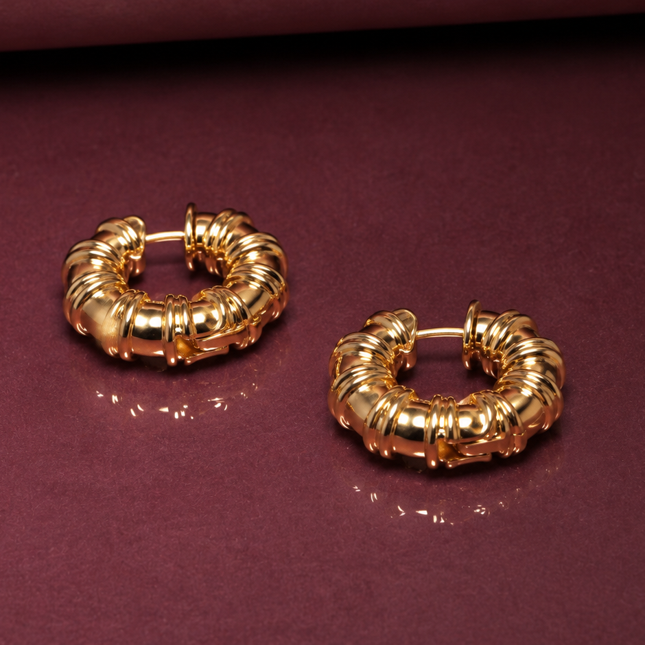 A pair of textured gold hoop earrings displayed on a dark burgundy surface.