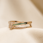 A gold ring with a small clear floral cluster and a green inlay, resting on draped cream-colored fabric.