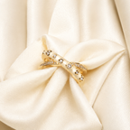 A gold ring with white enamel halo and small clear gemstones, displayed on a cream satin fabric background.