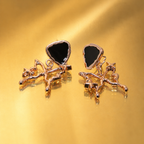 A pair of rose gold earrings featuring stylized cat figures with black heart-shaped inlays, displayed on a reflective gold surface.