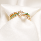 A delicate gold ring with a central cluster of small clear stones and two thin green inlay bands, displayed on soft white satin fabric.