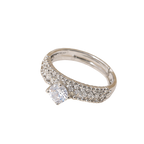 A silver-toned diamond ring with a single round-cut center stone and pavé-set side stones, shown on a plain white background.